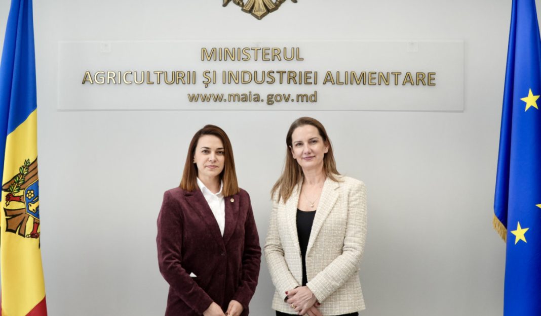 Two women in business attire stand before a government sign for the Ministry of Agriculture and Food Industry, with Moldova and EU flags on either side.