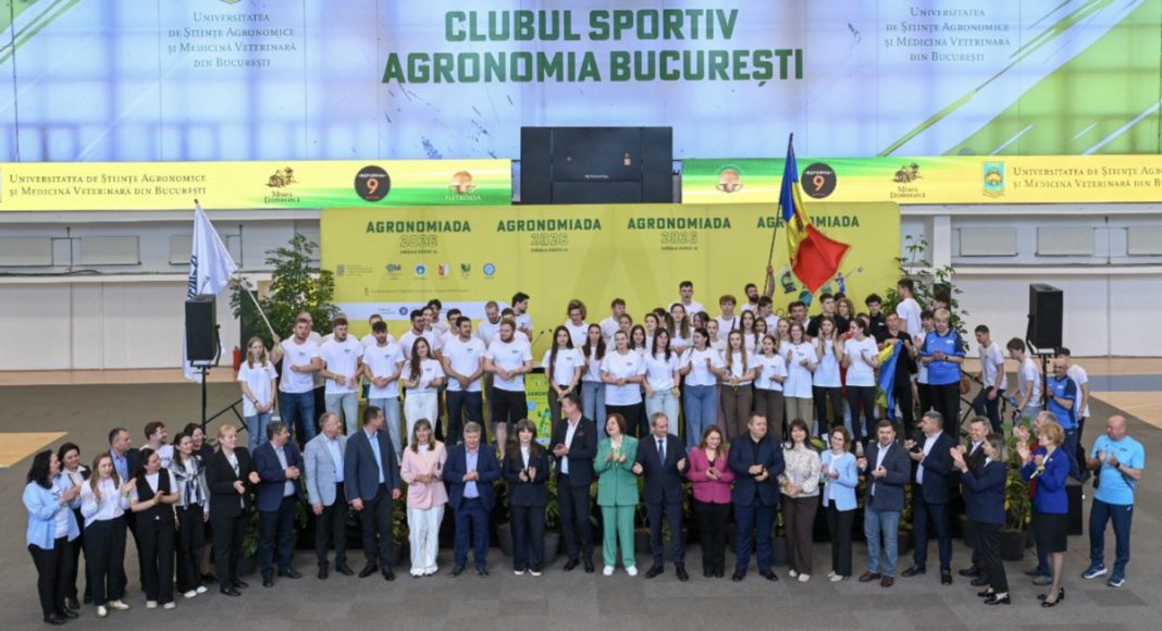 Group of students and officials on a stage at an agricultural university event in Bucharest, with a yellow 'AGRONOMIADA' banner and flags.