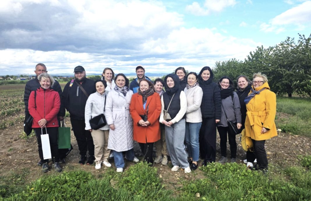 Group of diverse adults standing together in a farmland field on a cloudy day.