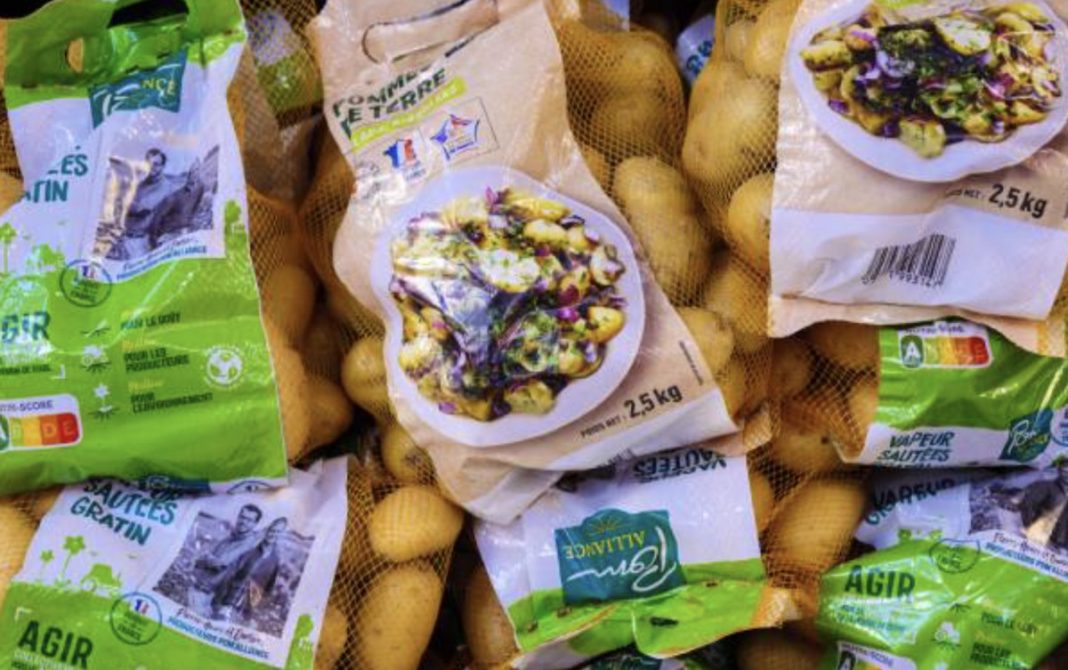 Bags of potatoes stacked together in green and beige packaging, some with images of potato salad on the front plate design.