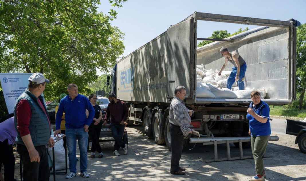 Group of volunteers unloading bags from a large truck in a sunny outdoor setting.