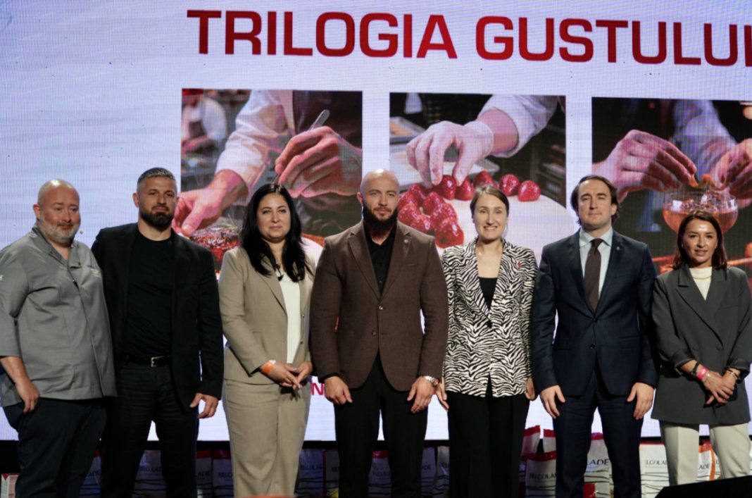 Seven people pose on a stage in front of a banner reading 'TRILOGIA GUSTULUI' on a large screen.