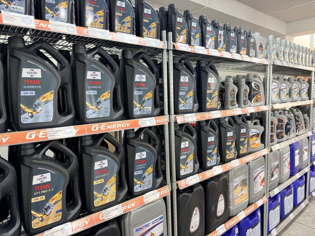 Rows of Titan Supersyn motor oil jugs on metal store shelves in a hardware/auto shop aisle.