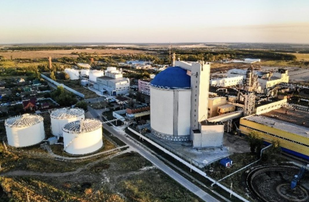Aerial view of an industrial facility with white storage tanks and a prominent blue-domed building, edges of roads and surrounding fields visible.