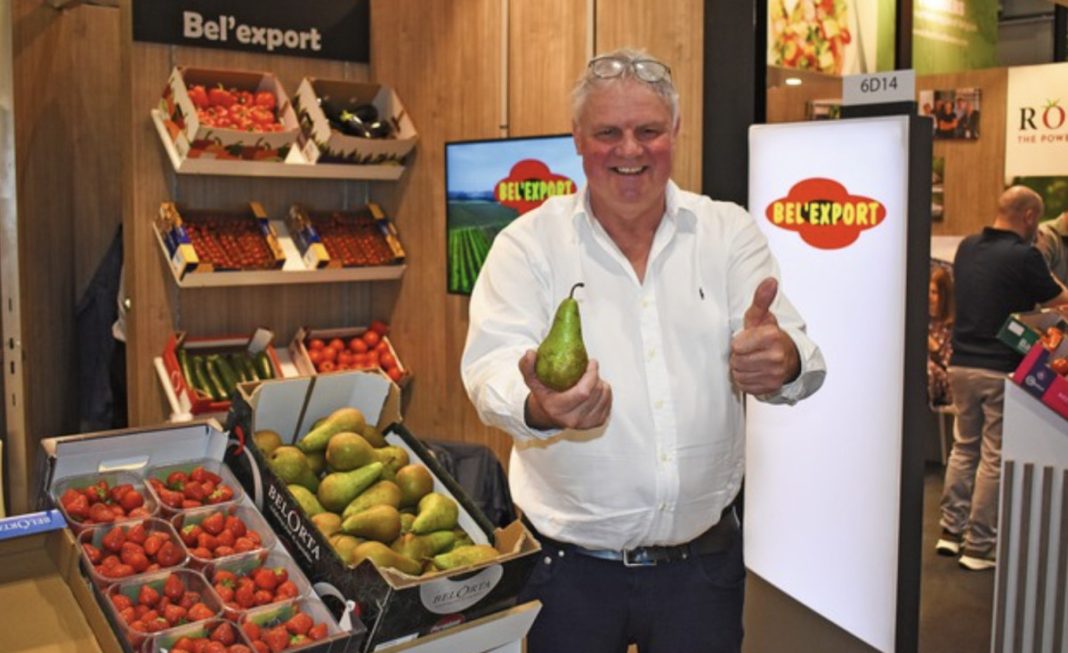 Smiling man at a trade show booth, holding a pear and giving a thumbs up.