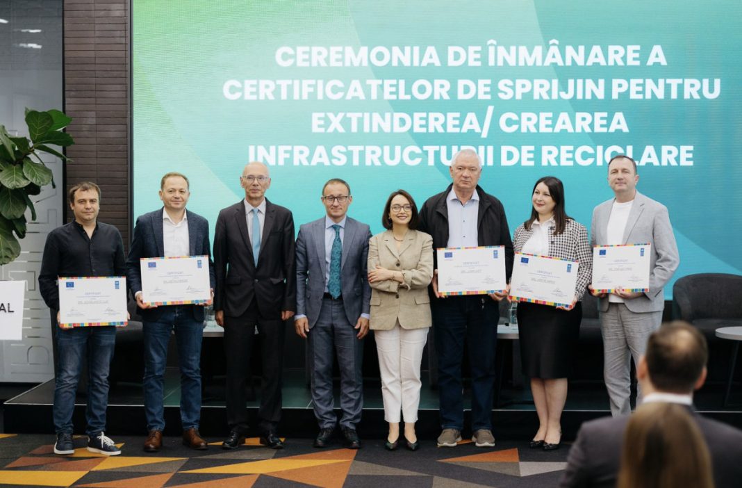 Eight people stand on a stage in business attire, each holding a certificate during a ceremony, with a large teal banner in Romanian behind them.