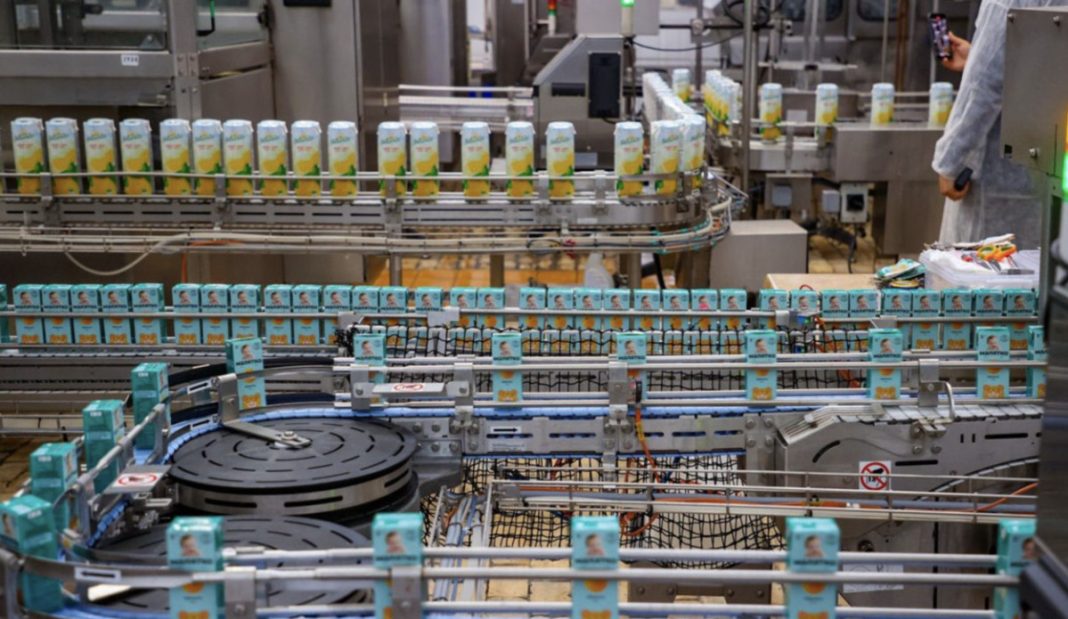 Automated beverage packaging line with blue-green cartons moving along conveyors in a factory.
