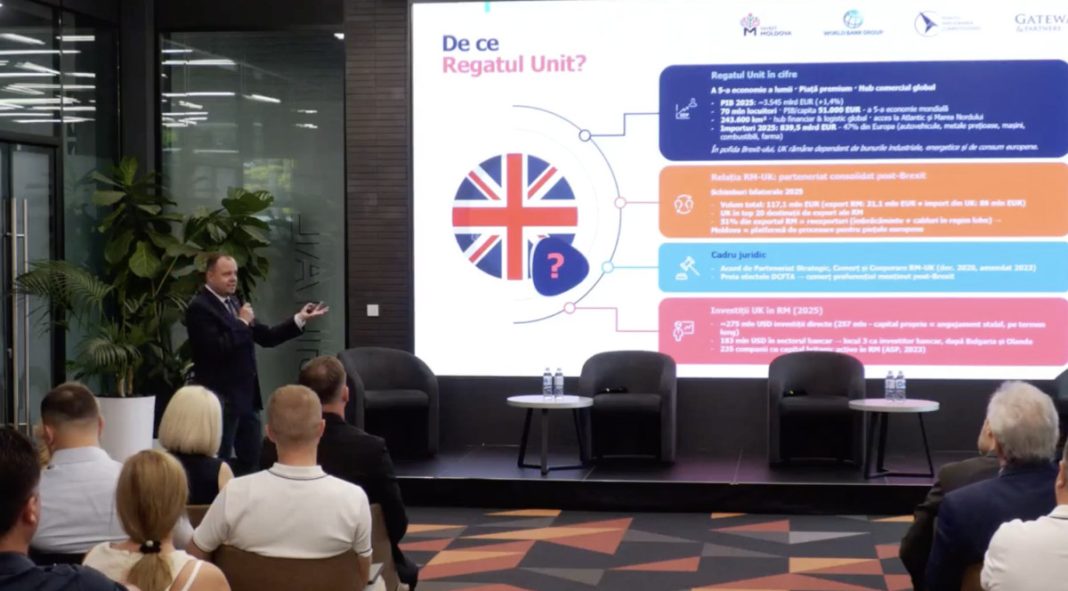 Speaker presenting on a stage with a large screen showing a UK-themed infographic and audience in a conference hall.