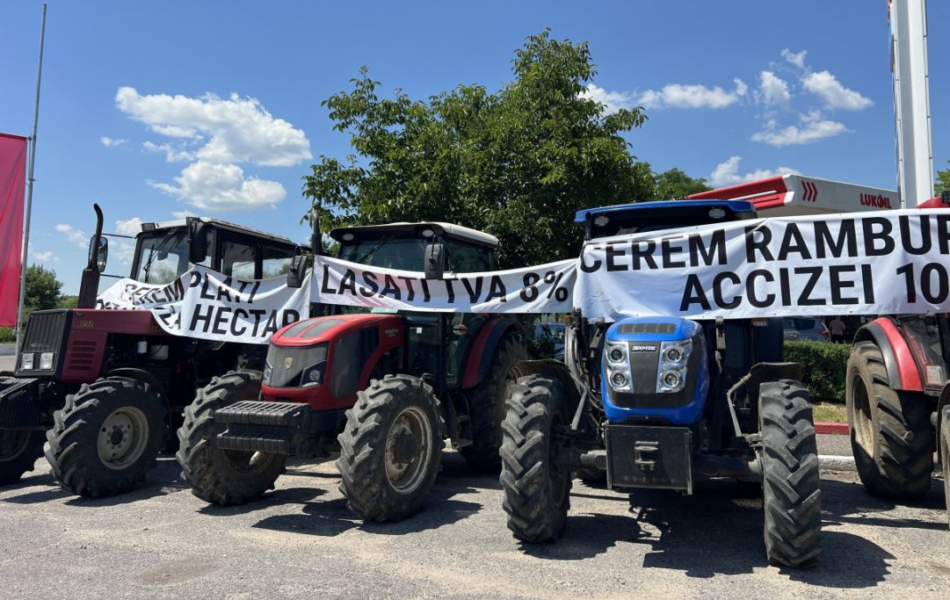 Row of tractors parked side by side with large protest banners across them on a sunny day; farmers protest about taxes and levies.